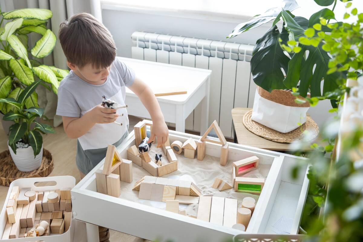 Little boy playing with wooden toys surrounded with plants and eco-friendly sustainable materials.