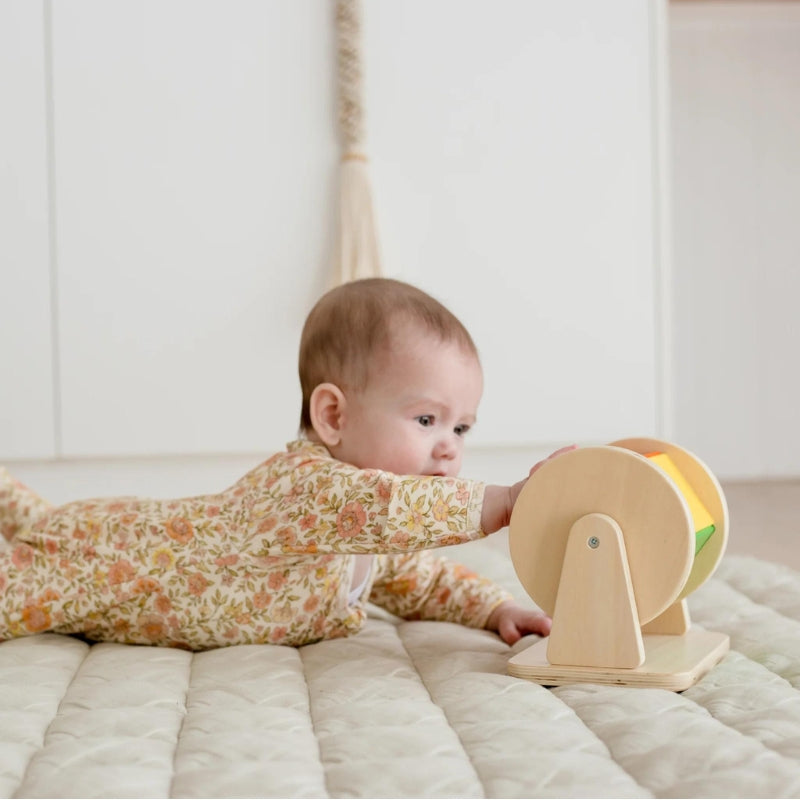 A baby playing with a developing toy called Montessori Spinning Drum.