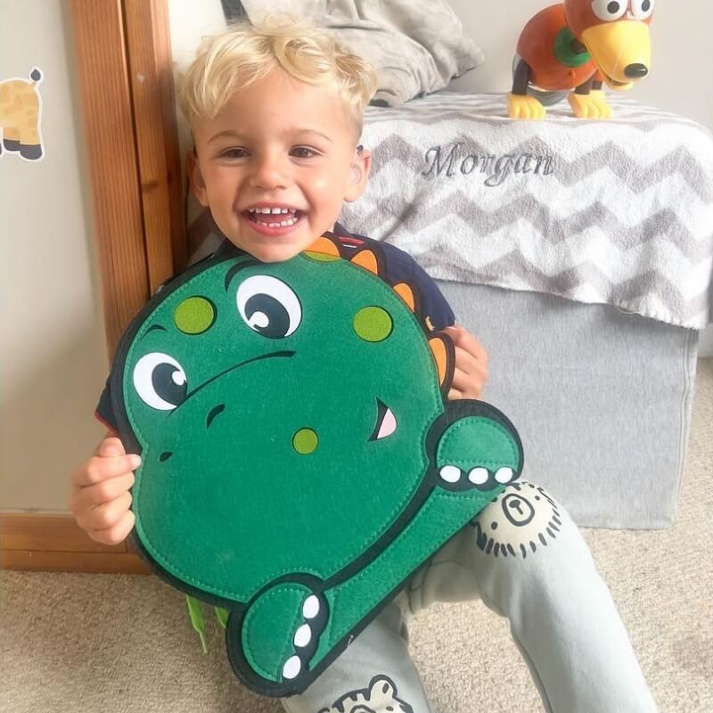 Blonde boy sitting, laughing, and hugging his Montessori Dino Busy Board