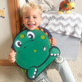 Blonde boy sitting, laughing, and hugging his Montessori Dino Busy Board