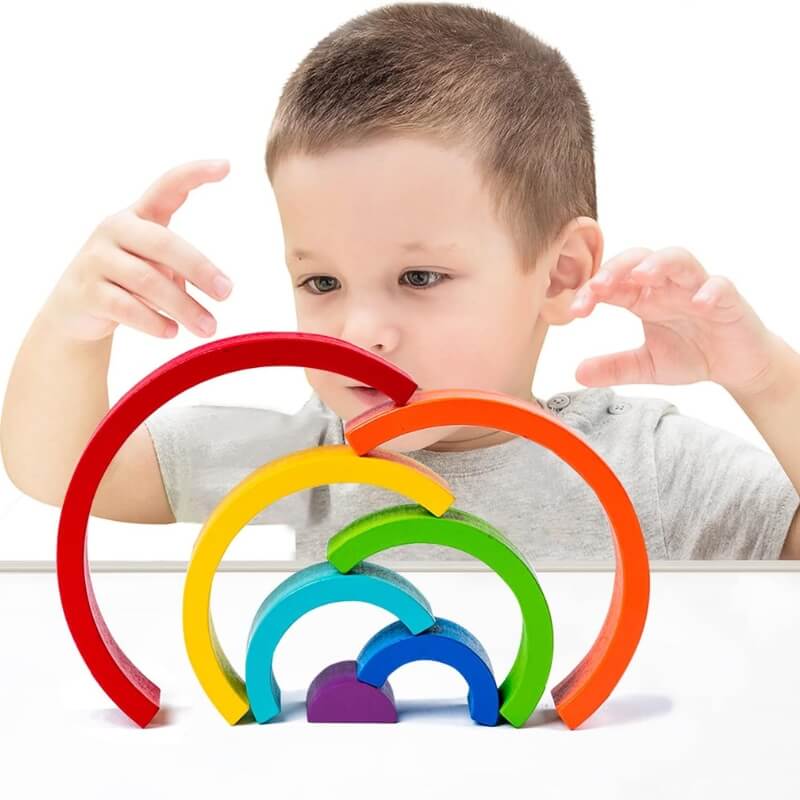 Little boy stacking Montessori rainbow pieces.