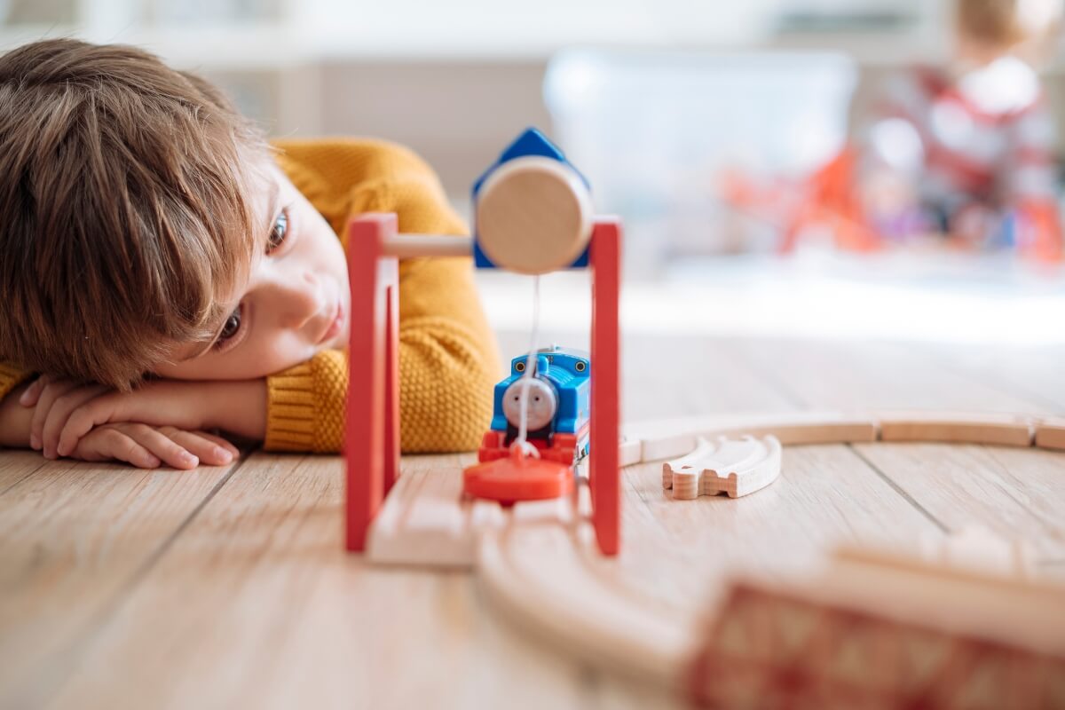 Little boy looking at a wooden train toy while laying on the floor. 