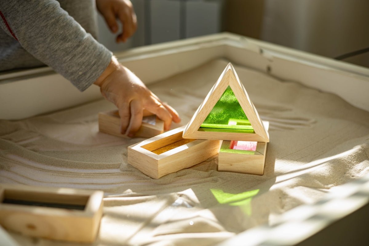 Baby playing with wooden toys in a sandbox.