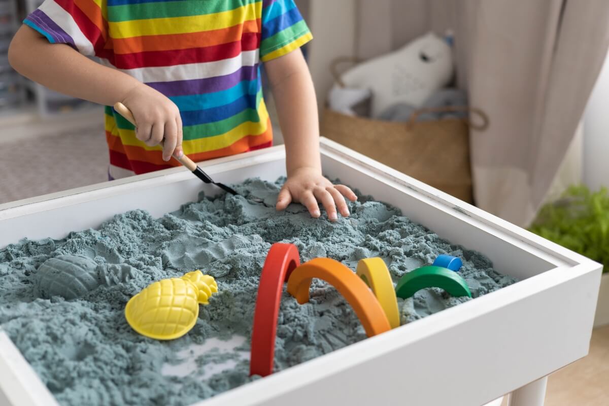 Boy playing with a sensory bin filled with blue sand and wooden toys.