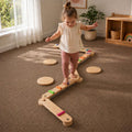 Child playing with a wooden balance beam toy in a playroom.
