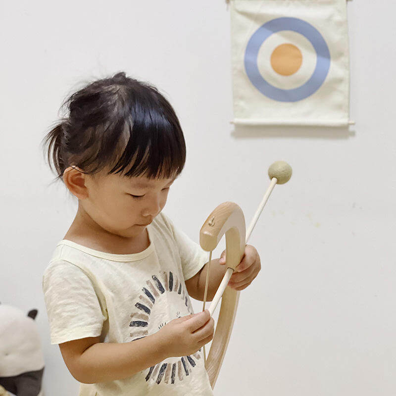 Little girl arming an arrow and preparing to shoot at a cloth target on the wall. 