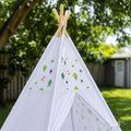 White kids teepee tent with wooden poles and cute forest animal prints set up outdoors in a sunny backyard.