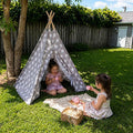 Two girls having a tea party and picnic in the backyard under a gray teepee tent. 