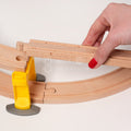 Wooden toy train track with a hand placing a wooden piece on it as part of the Montessori Crane and Train Magnetic Playset.
