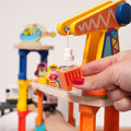 Child using the magnetic crane on a wooden construction train set to lift and move a toy cargo block.