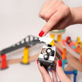 Woman's hand opening a battery compartment on the back of a white train featured in the Montessori Crane and Train Magnetic Playset, with the track visible in the background.