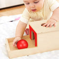 Baby playing with the Montessori Object Permanence Box, holding a red ball.