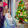 Mother, father, and daughter standing in front of a shop window looking at a Montessori Christmas Tree for children.